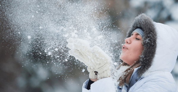 Девушка зимой дует на ладони снегом