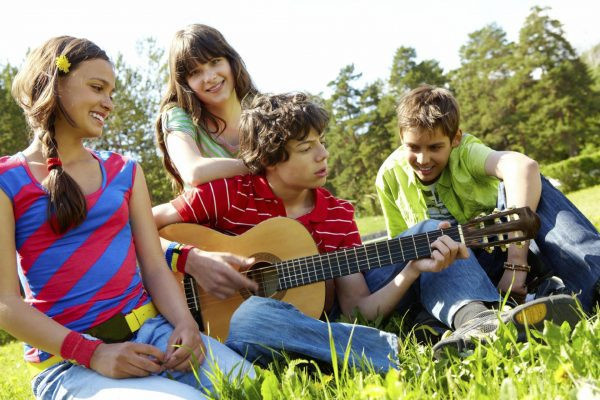 Компания подростков с гитарой сидит на траве