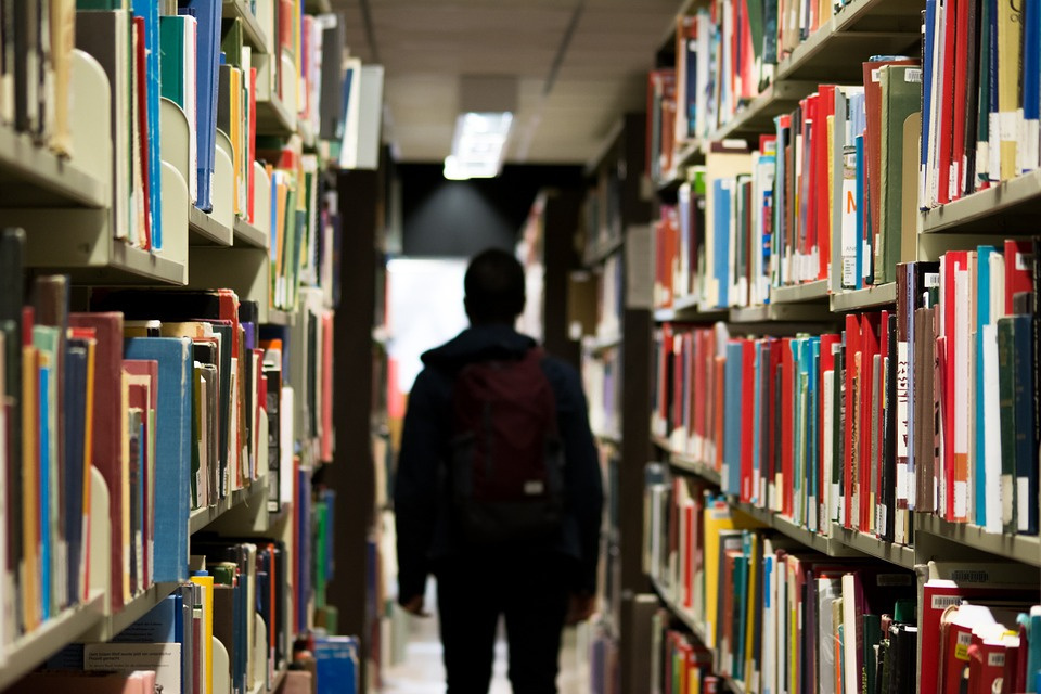 На фото студент в библиотеке среди множества книг.