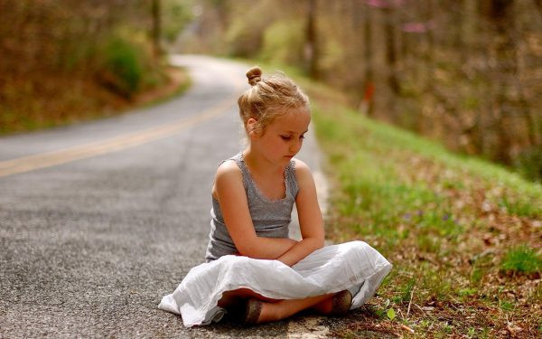 Маленькая девочка сидит на дороге